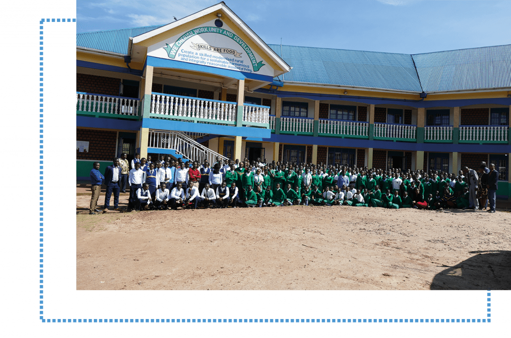 Großes Gruppenfoto von Schülern und Lehrern in grünen Uniformen vor dem Schulgebäude der St. Konrad Schule Uganda, das Motto „Skills are Food“ über dem Eingang.