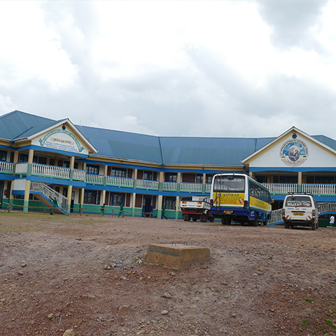 Frontansicht der St. Konrad Schule in Uganda, mit geparktem Schulbus im Vordergrund, der Schüler zur Schule bringt und die Erreichbarkeit unterstützt.