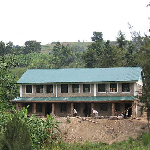 Zweistöckiges Schulgebäude an der St. Konrad Schule in Uganda, umgeben von grüner Natur, mit geräumigen Klassenräumen und Bauarbeitern, die an den Außenanlagen arbeiten.